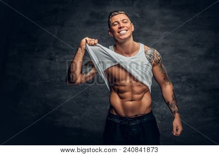 Studio Portrait Of Smiling, Athletic Male With A Tattoo On His Chest Ripping T Shirt.