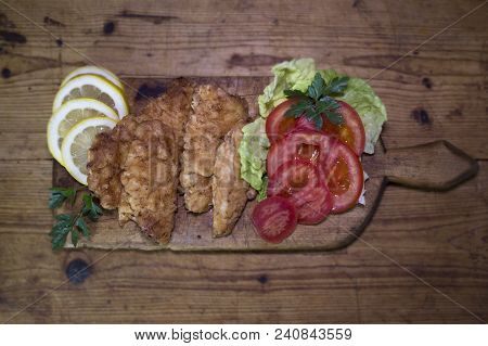 Breaded Chicken Meat With Salad And Lemon Resting On A Rustic Wooden Board