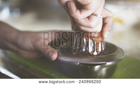 A Hand Squeezing Juice From An Orange On A Manual Glass Squeezer. Kitchen Background.