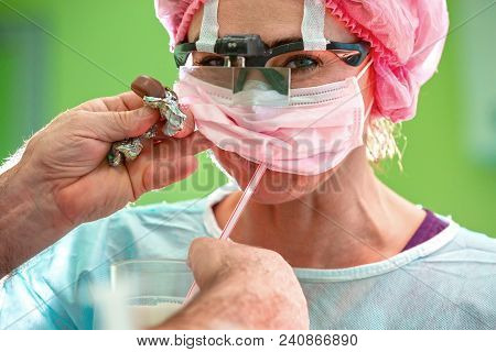 Female Sergeon Wearing In Mask And Hat Takes A Break With Coffee During Long Operation.
