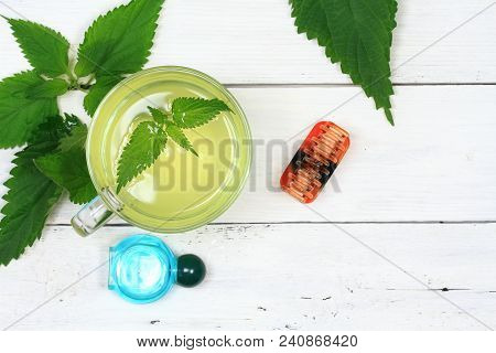Nettle Infusion  And Shampoon With Fresh Nettle Leaves On White Wooden Board.