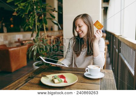 Woman Sitting Near Big Window In Coffee Shop At Table With Credit Card, Cup Of Coffee, Cake, Relaxin