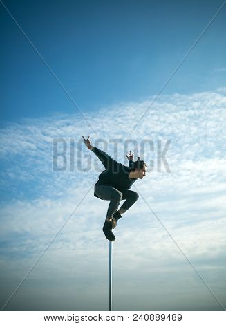 Strong Man Dancer Workout On Pole. Young Man Dancing On Pylon. Sexy Macho Man Fly On Blue Sky Backgr