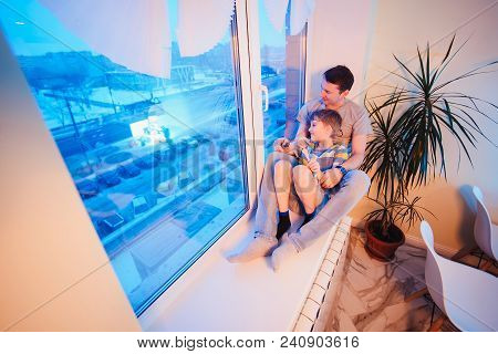 Parents And Kids Sitting Near Window And Having Fun At Kitchen. Father And Son On The Windowsill