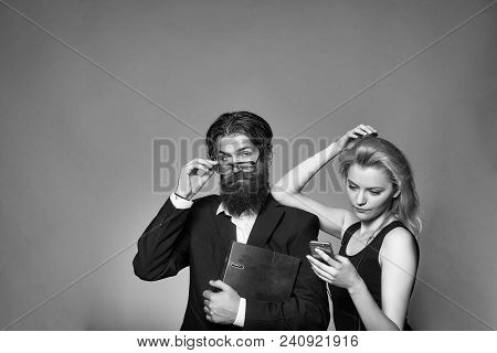 Serious Couple Of Young Blond Woman In Black Dress With Smartphone And Handsome Bearded Hipster Man 