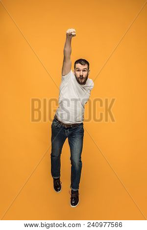 Freedom In Moving. Mid-air Shot Of Handsome Happy Young Man Jumping And Gesturing Against Orange Stu