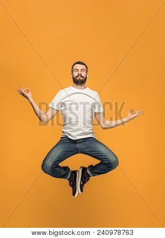 Freedom In Moving. Mid-air Shot Of Handsome Happy Young Man Jumping And Gesturing Against Orange Stu
