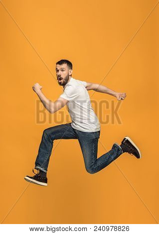 Freedom In Moving. Mid-air Shot Of Handsome Happy Young Man Jumping And Gesturing Against Orange Stu
