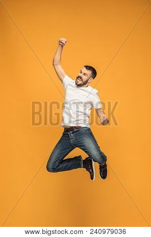 Freedom In Moving. Mid-air Shot Of Handsome Happy Young Man Jumping And Gesturing Against Orange Stu