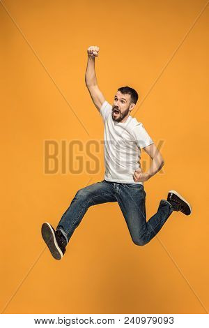 Freedom In Moving. Mid-air Shot Of Handsome Happy Young Man Jumping And Gesturing Against Orange Stu