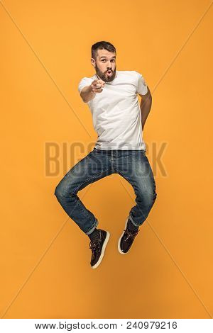 Freedom In Moving. Mid-air Shot Of Handsome Happy Young Man Jumping And Gesturing Against Orange Stu
