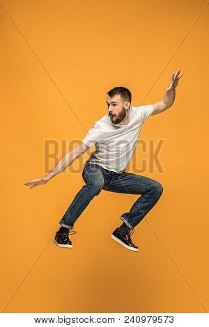 Freedom In Moving. Mid-air Shot Of Handsome Happy Young Man Jumping And Gesturing Against Orange Stu