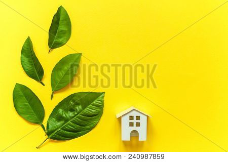 Miniature Toy Model House With Green Leaves On Yellow Colourful Trendy Backgdrop. Eco Village, Abstr