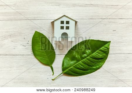 Miniature White Toy Model House With Green Leaves On Wooden Backgdrop. Eco Village, Abstract Environ