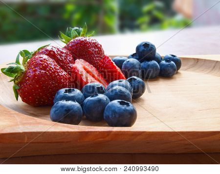 Fresh Whole, Half Strawberries And Blueberries On Wooden Bowl Outdoors. From The Side.