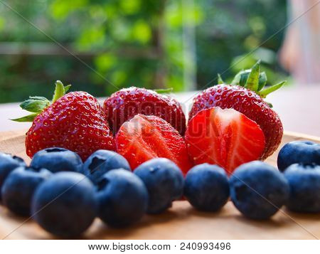 Fresh Whole, Half Strawberries And Blueberries On Wooden Bowl Outdoors. From The Front.
