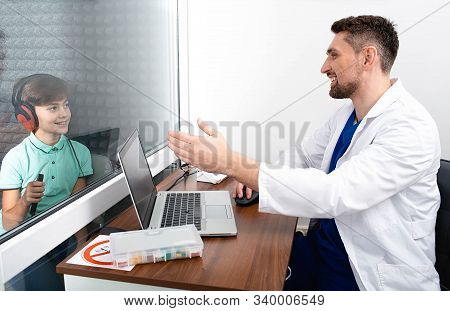 Audiometry Test. Cute Mixed Race Boy Sitting At Soundproof Cabin And Doing Hearing Test
