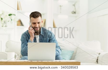 Young Man Using Laptop Having Phone Conversation, Working At Home, Panorama With Free Space