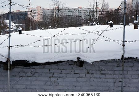 Depressing cityscape. Barbed wire and snow on roof of old brick shed.