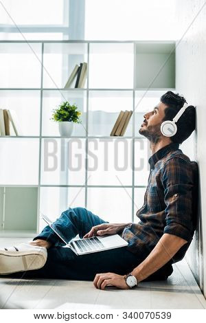Side View Of Handsome And Smiling Bi-racial Man With Laptop Listening Music