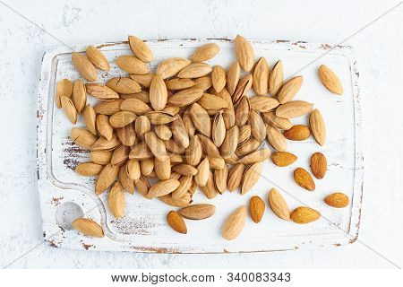 Top View Almonds In Endocarp, Bowl With Drupe In Shell On White Wooden Cutting Board. White Backgrou