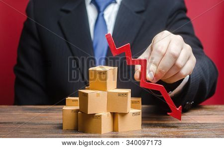 Businessman Is Holding A Red Arrow Down Above Boxes Stack Pile. Business Industrial Production Drop.