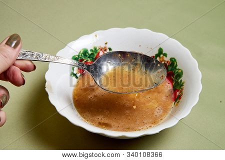 Raw Egg On A White Plate The Table, Small Spices In It And A Spoon In A Womans Handon. Cooking Eggs 