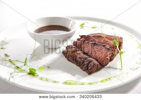 Alternative grilled skirt steak, well done machete fillet on white restaurant plate isolated. Macro shot of fresh juicy beef grillsteak, barbecue meat with brown spicy sauce and herbs closeup