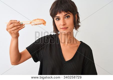 Beautiful woman eating salmon nigiri sushi using chopsticks over isolated white background with a confident expression on smart face thinking serious