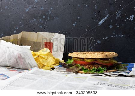 Delicious, Healthy Vegan Burger Placed On Old Vintage Newspaper With Chips On A Black Distressed Bac