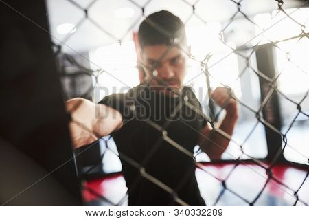 Blurred Picture. Strong Man Is Boxing In The Gym Behind The Fence. Haves Daily Exercise.