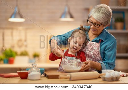 Happy loving family are preparing bakery together. Granny and child are cooking cookies and having fun in the kitchen. Homemade food and little helper.