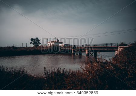 A Wide-angle Morning Misy Scenery With An Old Rusty Bridge And A Small River In The Middle, Dry Bush