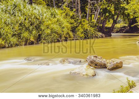River Flowing Beside Lush Green Trees & Plants In Rural Landscape Scene. Scenic Tropical Caribbean I