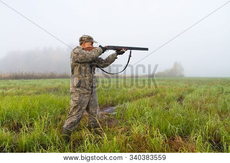 A Hunter Takes Aim With A Hunting Shotgun In A Meadow On A Foggy Morning At The Start Of A Hunt