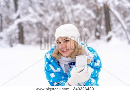 Beautiful Blonde Caucasian Woman In White Khitted Hat And Blue Blanket, Holding A Cup Of Coffee Or T
