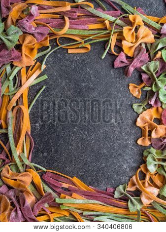 Frame Of Raw Pasta, Farfalle Bow-tie, Fettuccine Or Tagliatelle Colorful Pasta On Grey Background Wi