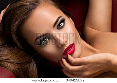 Beautiful seductive woman with dark brown eye makeup and bright red lips lying on the sofa