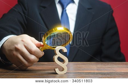 A Man Examines A Paragraph Figure With A Magnifying Glass. Studying Laws And Legislation, Norms, Rul