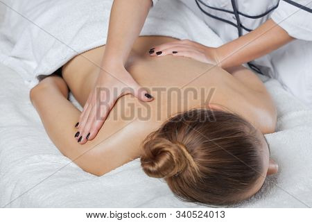 Masseur Makes A Relaxing Massage On The Neck, Shoulders And  Back Of A Young Beautiful Woman In A Sp
