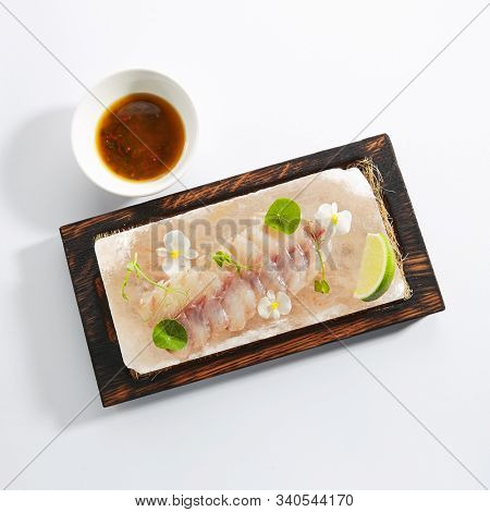 Sea perch ceviche or redfish cebiche on wood restaurant plate isolated. Macro photo of raw rockfish fillet marinated in lime juice with spicy sauce, edible flowers and greens top view