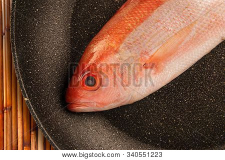 Red Snapper Raw Fish Isolated Disposed In A Fry Pan. Bamboo Table In Background.