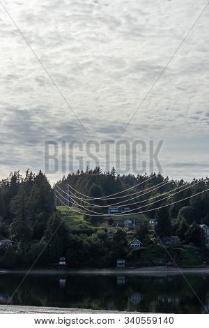Hillside With Homes And Forest With Communication And Power Lines Running Up Into A Cloudy Sky