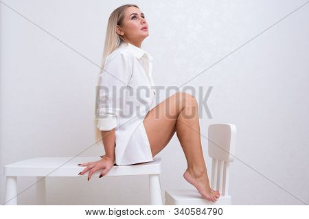 Beautiful Female In A White Shirt Sits On A Bench With Bare Legs. The Concept Of Skin Care, Hair