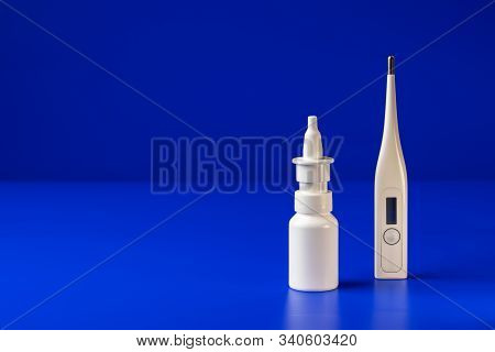 A White Bottle Without A Label For A Nasal Spray And A Thermometer For Measuring Body Temperature Ar