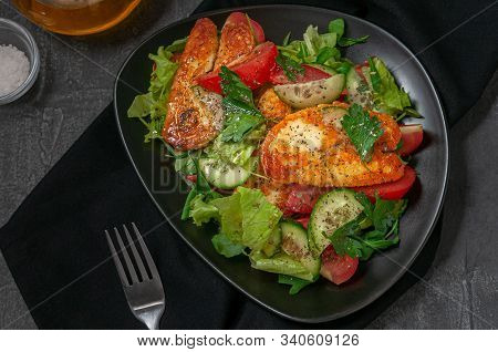 Salad With Vegetables And Fried Halumi Cheese With Spices. On A Black Plate. Next To The Plate Is A 