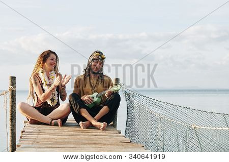 Cheerful Pretty Mature Woman With Flower Necklace Clapping To Her Husband Playing Ukulele When Thay 