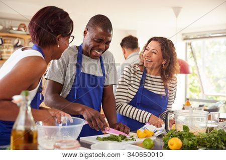 Male And Female Adult Students Preparing Ingredients For Dish In Kitchen Cookery Class