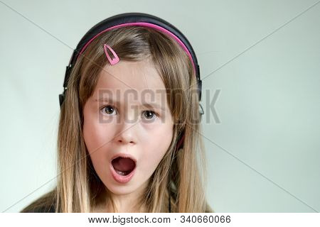 Pretty Smiling Cild Girl Listening To Music In Big Pink Earphones.