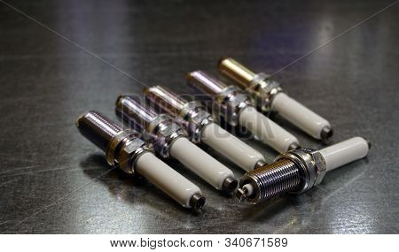 Spark Plugs For A Modern Engine On A Steel Background. Six Spark Plugs, One In Focus, The Rest In Th